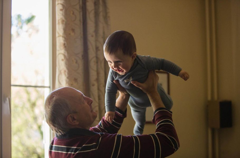 grandfather playing with young child indoors, by window